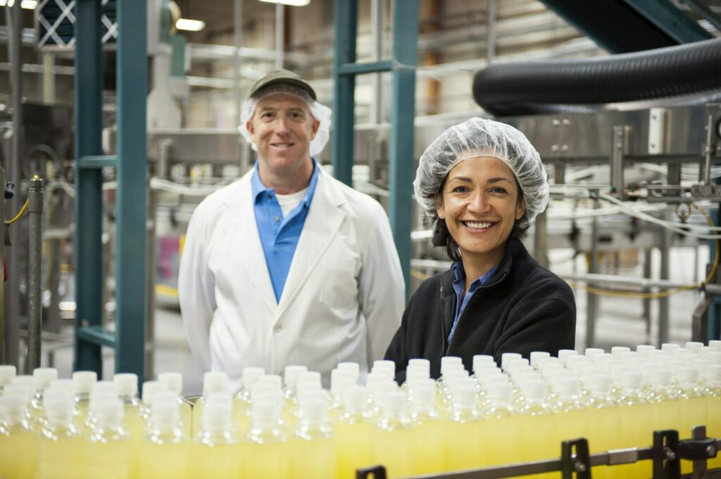 Workers wearing head nets and standing near a conveyor belt of bottles in a bottling plant.