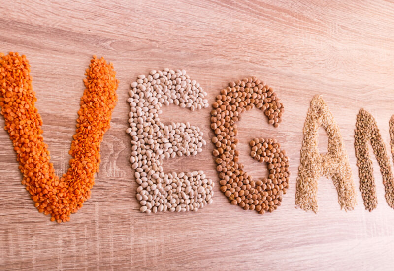 Word Vegan made of lentils, buckwheat, beans, rice and chickpeas on a wooden background